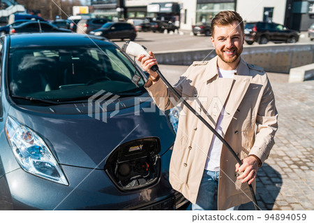 Portrait of stylish man with electric car charging connector in hands Portrait of stylish man with electric car charging connector in hands 94894059