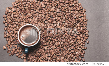 A cup of brewed black coffee on a dark background with beans. 94894579