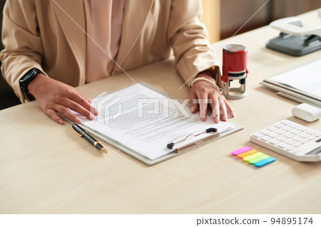 Close-up of young businesswoman examining business contract while working at her workplace at office Close-up of young businesswoman examining business contract while working at her workplace at office 94895174