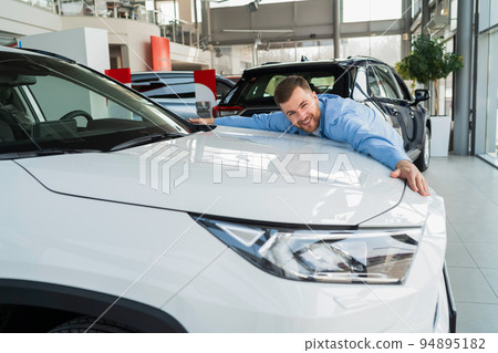 Handsome man hugging new car in dealership Handsome man hugging new car in dealership 94895182