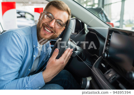 Satisfied man put his head on the steering wheel of his new car. Male in glasses in auto dealership Satisfied man put his head on the steering wheel of his new car. Male in glasses in auto dealership 94895394