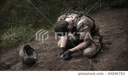 Sad soldier sits on the ground 94896783