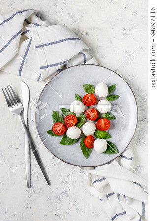 Caprese salad in the form of a Christmas tree. Festive tomato mozzarella and basil appetizer on light plate. Caprese salad in the form of a Christmas tree. Festive tomato mozzarella and basil appetizer on light plate. 94897116