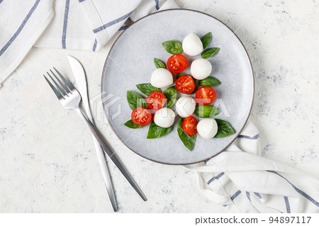 Caprese salad in the form of a Christmas tree. Festive tomato mozzarella and basil appetizer on light plate. Caprese salad in the form of a Christmas tree. Festive tomato mozzarella and basil appetizer on light plate. 94897117
