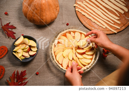 Top view of housewife, chef confectioner putting slices of apples on a raw pumpkin pie, preparing homemade traditional American classic tarte with crust lattice, for Thanksgiving Day. Autumn holidays 94897213