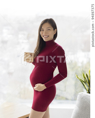 Asian pregnant woman showing 25 weeks pregnancy bump for maternity photoshoot holding wooden blocks sign happy. Vertical crop Asian pregnant woman showing 25 weeks pregnancy bump for maternity photoshoot holding wooden blocks sign happy. Vertical crop 94897375