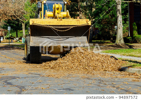 A bulldozer truck is tasked with cleaning up fallen leaves near homes during the autumn season by workers from municipalities over the entire city A bulldozer truck is tasked with cleaning up fallen leaves near homes during the autumn season by workers from municipalities over the entire city 94897572