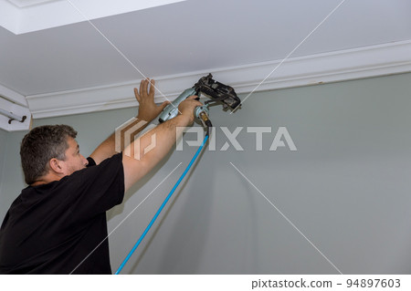 During the construction of a newly constructed home, this carpenter was nailing wooden crown molding between the ceiling and the wall During the construction of a newly constructed home, this carpenter was nailing wooden crown molding between the ceiling and the wall 94897603