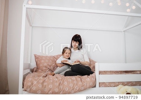 Caucasian preschooler girl and her young lady mother reading funny interesting children book 94897719