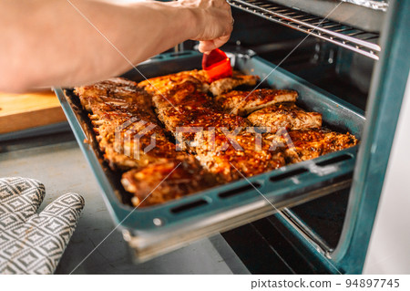 Woman cook taking out baked chicken from oven on baking sheet closeup Woman cook taking out baked chicken from oven on baking sheet closeup 94897745