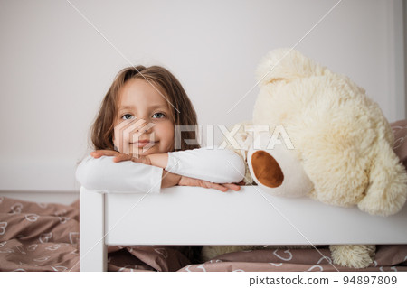 Health and beauty concept - little girl with teddy bear lying on bed at home. Health and beauty concept - little girl with teddy bear lying on bed at home. 94897809