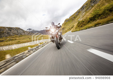 Motorcycle driver riding in Alpine highway. Motorcycle driver riding in Alpine highway. 94898908