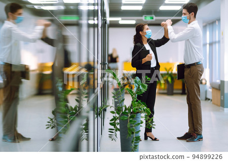 Business colleagues in protective masks in office bumping elbows while greeting each other at work. Business colleagues in protective masks in office bumping elbows while greeting each other at work. 94899226