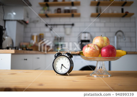 vintage alarm clock and fresh fruit on kitchen table intermittent fasting 94899339