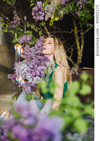 a blonde woman in a green top and jeans with lilac flowers.  a blonde woman in a green top and jeans with lilac flowers.  94900172