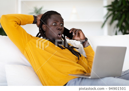 Unexpected News. Shocked Black Guy With Laptop Talking On Cellphone At Home Unexpected News. Shocked Black Guy With Laptop Talking On Cellphone At Home 94901501