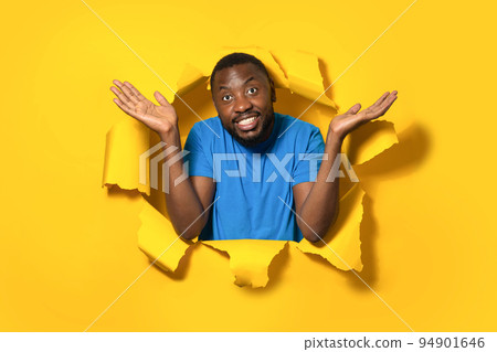 I don't know. African american man shrugging shoulders and spreading arms, standing in torn yellow paper hole I don't know. African american man shrugging shoulders and spreading arms, standing in torn yellow paper hole 94901646