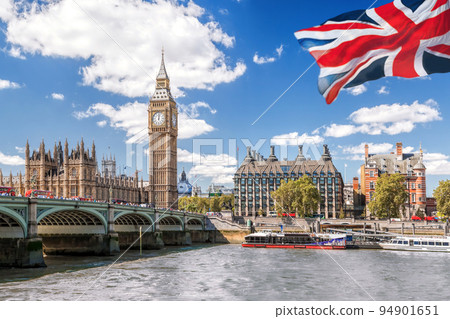 Big Ben with bridge over Thames and flag of England against blue sky in London, England, UK 94901651