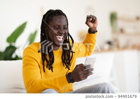 Online Win. Overjoyed Black Man Celebrating Success With Smartphone At Home 94901679