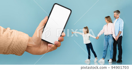 Cheerful young european man and woman with little girl pointing at huge smartphone with blank screen in hand 94901703