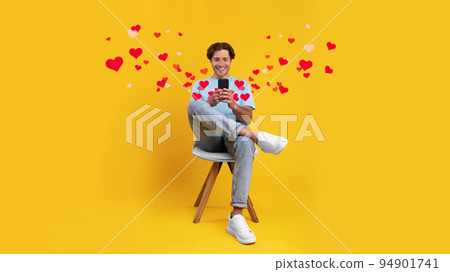 Happy guy using cellphone at studio, sitting on chair, chatting 94901741