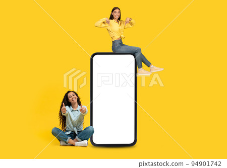 Happy european young woman sit on phone, have fun, show thumbs on big smartphone with blank screen Happy european young woman sit on phone, have fun, show thumbs on big smartphone with blank screen 94901742