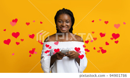 Portrait Of Happy Young Black Woman Holding Smartphone, Yellow Background Portrait Of Happy Young Black Woman Holding Smartphone, Yellow Background 94901786
