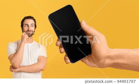 Pensive millennial european man look at huge smartphone with blank screen in hand Pensive millennial european man look at huge smartphone with blank screen in hand 94901787