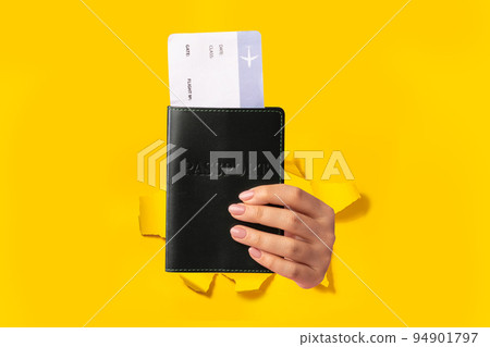 Tourist female hand holding passport with plane ticket isolated through torn yellow background, closeup 94901797