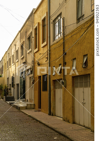 driveway, sidewalk and cobblestone in a small neighborhood, adjoining yellow and mustard-colored houses, at sunset driveway, sidewalk and cobblestone in a small neighborhood, adjoining yellow and mustard-colored houses, at sunset 94902363