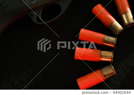 Trigger of a rifle on black background with red lightning with Shotgun shells on a black surface. Ammunition for 12 gauge smoothbore weapons. Hunting ammunition. Dark background. Trigger of a rifle on black background with red lightning with Shotgun shells on a black surface. Ammunition for 12 gauge smoothbore weapons. Hunting ammunition. Dark background. 94902644