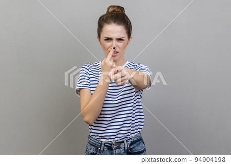 Hey, you are liar. Portrait of woman wearing striped T-shirt standing with upset disappointed face and touching nose, showing lie gesture. Indoor studio shot isolated on gray background. Hey, you are liar. Portrait of woman wearing striped T-shirt standing with upset disappointed face and touching nose, showing lie gesture. Indoor studio shot isolated on gray background. 94904198