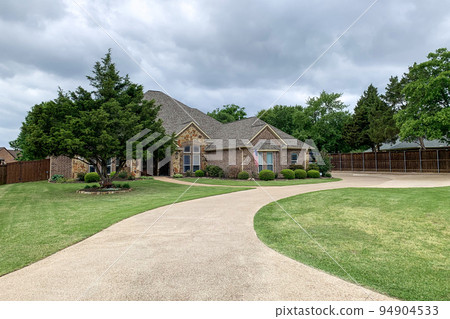 Brand new residential houses with concrete driveway and asphalt road in front, road leading to a house with a lawn with bushes and trees in front. Real estate. 94904533