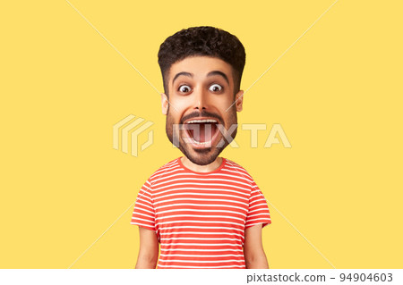 Caricature comic portrait of surprised funny young adult man looking at camera with open mouth and amazed big eyes, expressing astonishment. Indoor studio shot isolated on yellow background 94904603