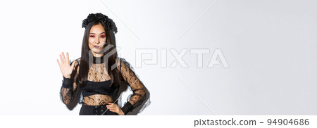 Image of confident beautiful asian woman in halloween costume showing five fingers, raising hand to say hello, standing over white background Image of confident beautiful asian woman in halloween costume showing five fingers, raising hand to say hello, standing over white background 94904686