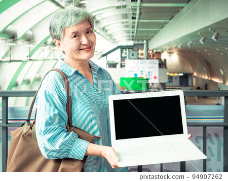 A 60-year-old Asian elderly woman smiles in public when she displays a blank screen, writes a video screen, and uses a blank screen to create an advertisement. 94907262