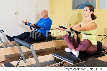 Woman pulling stretch band sitting on pilates training machin 94911485