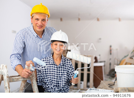Portrait of builder boy together with his father with paint rollers in room being renovated 94911676