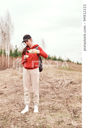 A beautiful girl in a cap travels through spacious fields and meadows, drinks a thermos. 94912222