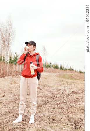 A beautiful girl in a cap travels through spacious fields and meadows, drinks a thermos. A beautiful girl in a cap travels through spacious fields and meadows, drinks a thermos. 94912223