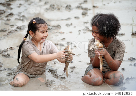Two happy children child girl catching big frog in the large wet mud puddle on summer day. Two happy children child girl catching big frog in the large wet mud puddle on summer day. 94912925