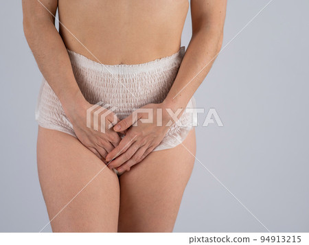 A woman in adult diapers holds her hands on her stomach. Urinary incontinence problem. 94913215