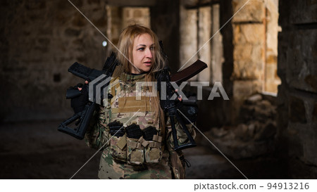 Blonde woman in army uniform holding a firearm in an abandoned building. Blonde woman in army uniform holding a firearm in an abandoned building. 94913216