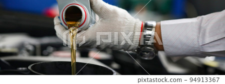 Auto mechanic in gloves pour engine oil into engine Auto mechanic in gloves pour engine oil into engine 94913367
