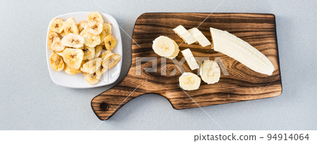 Banana slices on a cutting board and banana chips on a saucer on the table. Fast food. Web banner Banana slices on a cutting board and banana chips on a saucer on the table. Fast food. Web banner 94914064