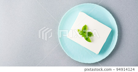 A piece of fresh feta cheese and basil leaves on a plate on the table. Ingredient for Greek salad. Top view. Web banner. Copy space A piece of fresh feta cheese and basil leaves on a plate on the table. Ingredient for Greek salad. Top view. Web banner. Copy space 94914124