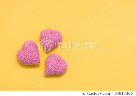 Handmade for Valentine's Day. Three knitted pink hearts on a yellow background. Copy space 94914306