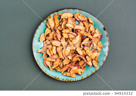 Pieces of dry apples on a plate on a green background. Healthy eating. Top view 94914332