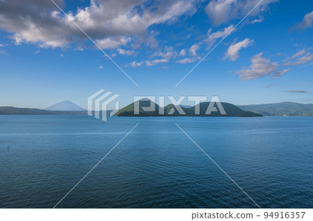 The surface of Lake Toya reflecting the blue sky and flowing clouds 94916357