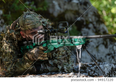 A military man or airsoft player in a camouflage suit sneaking the river and aims from a sniper rifle to the side or to target. 94917220